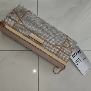 Glittrig kuvertväska från River Island - Snygg kuvertväska från River Island med glittriga silverdetaljer och geometriskt mönster i guld. Väskan har en elegant rektangulär form, guldfärgad kant och en liten metallögla för att hålla i. Perfekt för att lyfta din outfit med extra bling.