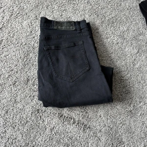 Tiger of Sweden svarta jeans 28/30 - Snygga svarta jeans från Tiger of Sweden i storlek 28/30. Modellen har klassisk femficksdesign, raka ben och twillväv. Perfekt passform med normal midja och stilren look. Passar dig som gillar minimalistisk och modern stil.