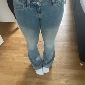 Low waist jeans  - Säljer ett par ljusblå bootcut jeans med snygga slitningar och cool fickdetalj bak. Jeansen har klassisk femficksdesign, knapp och dragkedja framtill samt bälteshällor. Passformen är normal och materialet är mjukt jeans. Perfekt för dig som gillar retrovibbar och vill sticka ut.