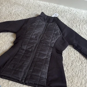 Svart quiltad jacka Fairfield XS ridjacka - Svart Camarine jacka från Fairfield Equestrian i storlek XS. Snyggt quiltad framsida och rygg med dragkedja hela vägen, ribbade och stickade partier på sidor och ärmar för extra komfort. Perfekt för dig som gillar stilren och sportig look.