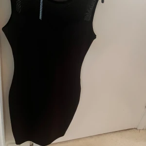 Svart tight ärmlös kortklänning - Det Snygg svart kortklänning med tight passform och ärmlös design. Klänningen har en stilren look med meshdetaljer upptill som ger en cool touch. Perfekt för dig som gillar minimalistisk stil och vill ha något som sitter snyggt och markerar figuren.