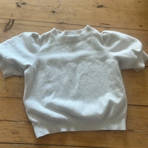 Ljus beige tröja  - Superskön ljusbeige stickad tröja från Vero Moda med puffiga korta ärmar och ribbade muddar vid hals, ärmslut och nederkant. Perfekt för dig som gillar en enkel men ändå trendig look. Materialet är mjukt och har en lite texturerad yta.