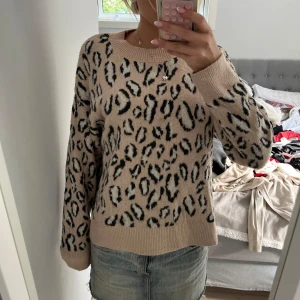 Beige leopardmönstrad stickad tröja - Säljer en beige stickad tröja med svart leopardmönster. Tröjan har ribbade muddar vid ärmslut och nederkant. Perfekt för dig som gillar djurmönstee och vill ha en mysig och trendig look.🥰🤗