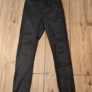 Svarta leggings med scrunch-detalj - Snygga svarta leggings med glansig finish och scrunch-detalj bak som framhäver formen. Hög midja och tight passform. 