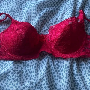 Röd spetsig bh med rosett - Snygg röd korsett med spetsdetaljer och en liten rosett framtill. Kuporna är vadderade och har blommigt spetsmönster som ger en lyxig vibe. Axelbanden är justerbara för perfekt passform. Perfekt för dig som vill ha något extra.