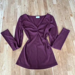 Vinröd ribbad klänning från Vila - Snygg vinröd kortklänning från Vila med ribbad struktur och v-ringad hals. Klänningen har långärmade ärmar och en twistad detalj framtill som ger en cool siluett. Perfekt för dig som gillar stilrena och trendiga plagg med lite edge. Noppror här och var förekommer 