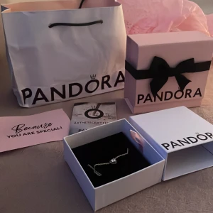 Pandora halsband med hjärthänge - Supersött halsband från Pandora i silver med ett gnistrande hjärthänge dekorerat med små stenar. Kedjan är tunn och elegant, perfekt för att ge din look lite extra shine. Kommer i originalask med certifikat och presentpåse.