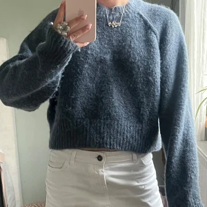 Blå croppad stickad tröja - Mysig croppad stickad tröja i mörkblå ton med långärmade raglanärmar och ribbade muddar.