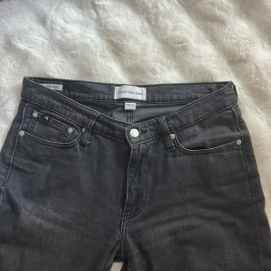 Svarta jeans från Calvin Klein - Snygga svarta jeans från Calvin Klein med klassisk femficksdesign och silverfärgade nitar. Jeansen har en rak passform och normal midja, med CK-logga på bakfickan. Materialet är mjukt denim i bomull med lite stretch för extra komfort.