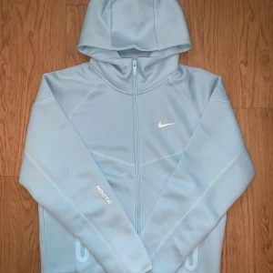 Blå NOCTA x Nike hoodie M - Säljer en ljusblå hoodie från NOCTA x Nike i storlek M. Tröjan har NOCTA-logga tryckt på framsidan och klassisk Nike Swoosh. Mjukt material med ribbade detaljer och huva. Perfekt för dig som gillar streetwear och snygga detaljer. Passar en S bättre 