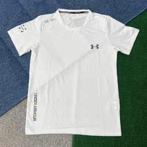 Vit t-shirt från Under Armour - Snygg vit t-shirt från Under Armour med tryckt logga på bröstet och text på ärmen och nedre sidan. T-shirten har rund hals och är gjord i ett lätt och funktionellt syntetmaterial som passar perfekt för träning. Klassisk kortärmad modell med sportig vibe.