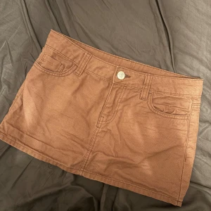 Brun jeanskjol med fickor - Snygg brun kort jeanskjol med klassiska fickor fram och bak, samt silverfärgade knappar. Kjolen har bälteshällor och är tillverkad i ett stadigt bomullsmaterial. Perfekt för dig som gillar en enkel och cool stil.