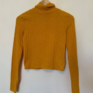 Gul polotröja från H&M - Säljer en snygg gul ribbad polotröja från H&M. Tröjan har långa ärmar och en bekväm passform.