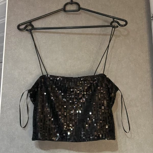 Svart paljettprydd tubtopp från Gina Tricot - Säljer en snygg svart tubtopp från Gina Tricot, täckt med glittrande paljetter. Toppen har tunna axelband och en croppad passform, aldrig använd 
