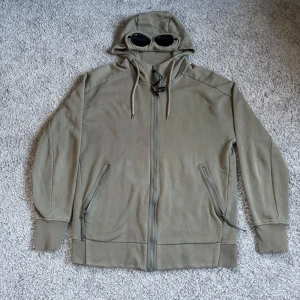C.P. Company tröja  - Säljer en beige huvtröja från C.P. Company med dragkedja och huva med inbyggda glasögon. Tröjan har långa ärmar och praktiska fickor med dragkedja. Perfekt för en stilren och unik look. Priset går att diskutera! Hör gärna av er vid frågor och funderingar! MVH Lavish