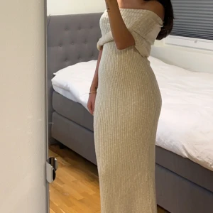 Beige ribbad offshoulder klänning - Snygg beige ribbad klänning med offshoulder-design. Perfekt för en stilren look med sin långa längd och figurnära passform. Klänningen är både bekväm och trendig. går att ha på 2 olika sätt