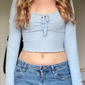 Ljusblå ribbad croppad topp - Säljer en ljusblå ribbad croppad topp med långa ärmar och knytning framtill. Perfekt för en avslappnad stil. Passar bra till jeans eller kjol.