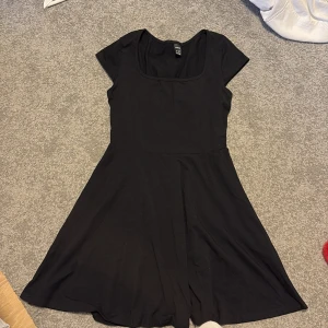 Svart kortklänning - Säljer en stilren svart kortklänning. Klänningen har korta ärmar och en rund halsringning, perfekt för en enkel och elegant look. Materialet är mjukt, tunt och bekvämt. 