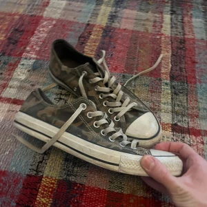 Camouflage sneakers från Converse - Säljer ett par coola Converse sneakers i camouflage-mönster. Skorna har klassisk snörning och en vit sula med svart rand. Perfekta för en avslappnad stil.