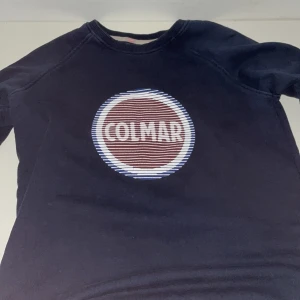 Mörkblå tröja från Colmar - Säljer en snygg mörkblå tröja från Colmar med deras ikoniska logga på bröstet. Tröjan har långa ärmar och en rund halsringning. Perfekt för en avslappnad stil.