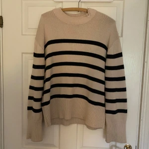 Beige och svart randig stickad tröja - Säljer en snygg beige stickad tröja med svarta ränder. Tröjan har långa ärmar och en rund halsringning. Perfekt för kyligare dagar!