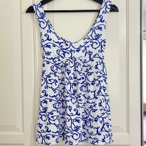 Sommrig knyttopp - Superfin topp ifrån onto moda. Toppen är ärmlös med lite tjockare axelband och knytning som går att ha båda fram eller baktill. Linnet har jättesnyggt klarblått mönster och en lösare passform💘