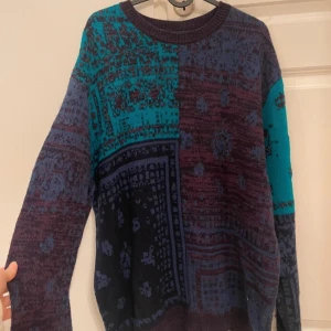 Mönstrad stickad tröja från Topman - Säljer en unik stickad tröja från Topman med ett coolt mönster i blått, lila och turkos. Tröjan har en normal passform och långa ärmar, perfekt för att hålla sig varm och stilren under kyligare dagar.