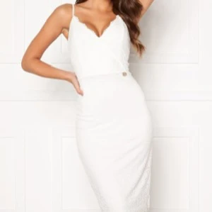 Vit spetsklänning  - Elegant vit klänning i spets med v-ringad design och smala axelband. Perfekt för sommaren eller som studentklänning. Klänningen har en figurnära passform men är ’stretchig’ och anpassas därför fint efter kroppen.