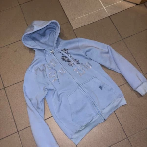 Ljusblå hoodie från Vonstudio - Säljer en ljusblå hoodie från Vonstudio med dragkedja och glittriga detaljer på framsidan. Tröjan har en mysig huva och långa ärmar. Perfekt för en avslappnad stil. 💙