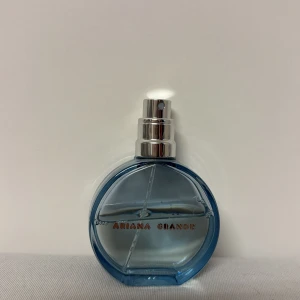 Parfym från Ariana Grande - En elegant parfymflaska i blått glas med en rund form och silverfärgad spraypump. Flaskan har en modern design med namnet 'Ariana Grande' i guldtext på framsidan. Perfekt för den som älskar en fräsch och ungdomlig doft.