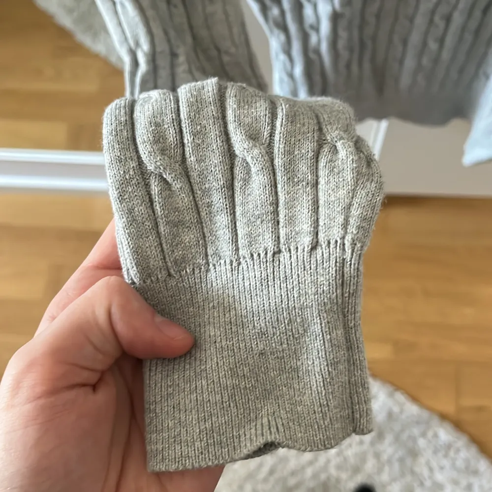 Säljer en stilren grå stickad tröja från GANT i stretchig bomull. Tröjan har ett klassiskt kabelstickat mönster och rund halsringning. Perfekt för en avslappnad men ändå snygg look. 🧶. Neuletakit & Villapaidat.