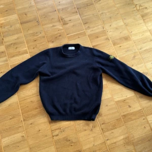 Mörkblå stickad tröja från Stone Island - Säljer en snygg mörkblå stickad tröja från Stone Island. Tröjan har en rund halsringning och ett ikoniskt märke på ärmen. Perfekt för kyligare dagar och ger en stilren look. Har kvitto från NK och pris tagg.