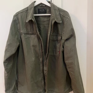 Jacka från Indicode - Säljer en olivgrön jacka från Indicode med dragkedja framtill och två bröstfickor med lock. Jackan har en klassisk krage och långa ärmar. Perfekt för en avslappnad stil och perfekt till våren/ sommaren. Jackan är knappt använd så den är i mycket bra skick. 