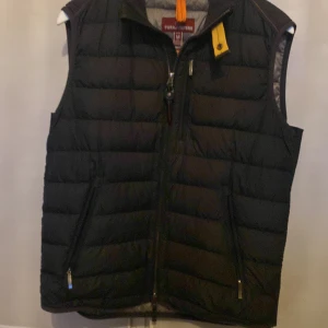 Svart dunväst från Parajumpers - Säljer en svart dunväst från Parajumpers i storlek M. Västen har en dragkedja framtill och är superlätt. Perfekt för lager-på-lager under kyliga dagar. Märket är känt för sin kvalitet och hållbarhet.