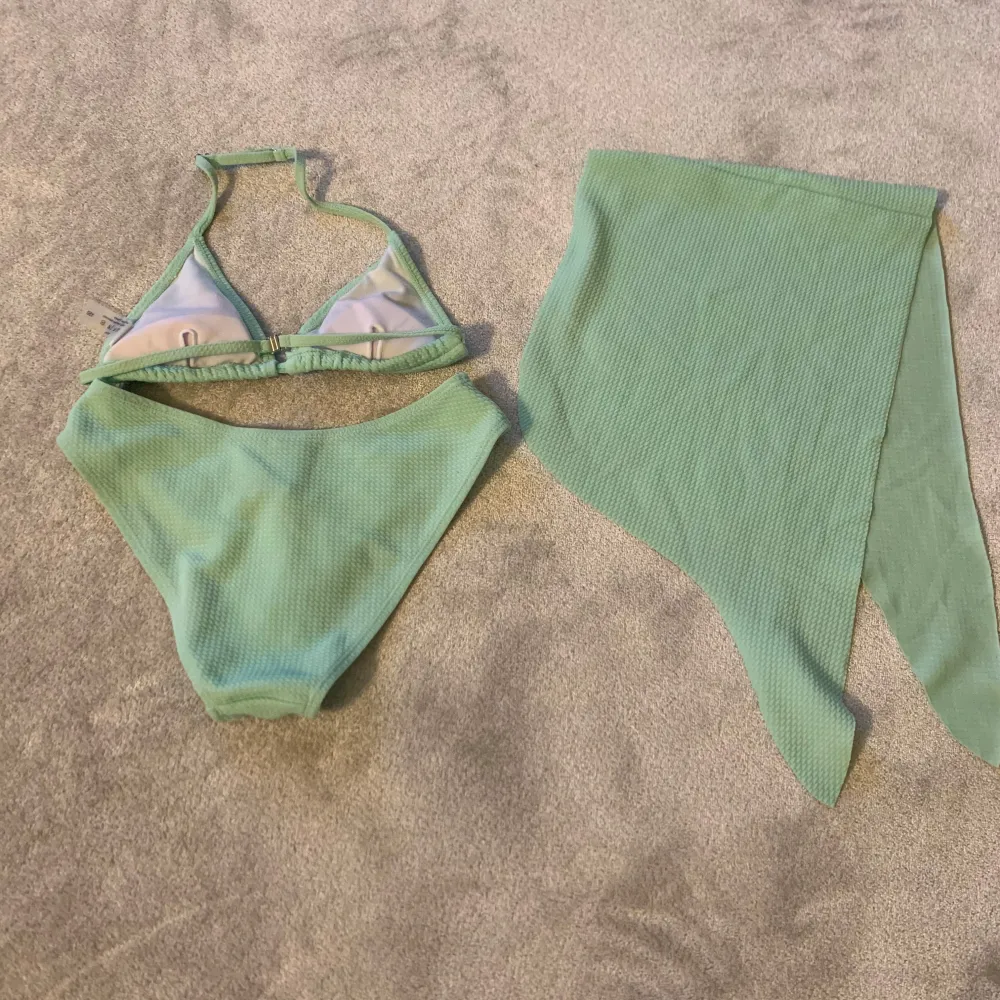 Snygg mintgrön bikini med trekantsöverdel och matchande kjol. Bikinin har knytband i nacken och en ribbad textur som ger en trendig look. Perfekt för sommarens stranddagar!. Muu.