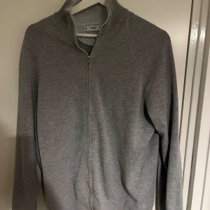 Grå kofta från Mango - Säljer en stilren grå kofta från Mango med dragkedja framtill. Perfekt för lager-på-lager under kyligare dagar! Andvänd ett fåtal gånger! 