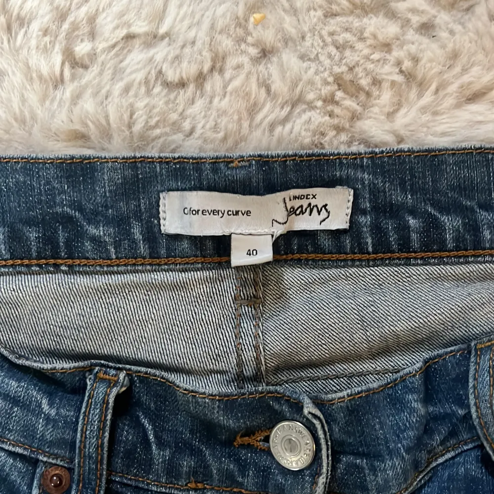 Säljer ett par klassiska blå jeans från Lindex. De har en blandning mellan rak och bootcut passform med femficksdesign och knappgylf. Perfekta för en avslappnad stil. Jeansen har tyvärr ett hål på båda sidorna som syns på sista bilden men går super enkelt att fixa med lite nål och tråd! Original priset ligger mellan 400-700kr.. Farkut & Housut.