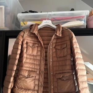 Beige dunjacka från Moncler - Säljer en snygg beige dunjacka från Moncler. Jackan har en quiltad design med långa ärmar och praktiska fickor med knappar! 