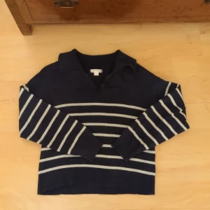 Mörkblå randig tröja Gina Tricot  - Säljer en snygg mörkblå tröja med vita ränder. Tröjan har en krage och långa ärmar, perfekt för en stilren look. Den är tillverkad i ett mjukt material som känns skönt mot huden.