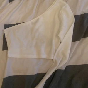 Vit oneshoulder topp - Säljer en stilren vit oneshoulder topp. Perfekt för en trendig look med sin unika design. Toppen är ribbad och har en tight passform som framhäver figuren.