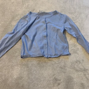 Blå kofta med knappar - Säljer en enkel och stilren blå kofta med knappar framtill. Koftan har långa ärmar och en klassisk passform. Perfekt för lager-på-lager under kyligare dagar.