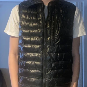 Svart dunväst med dragkedja från peak performance  - Säljer en stilren svart dunväst med dragkedja. Västen har en hög krage och flera praktiska fickor med dragkedjor. Perfekt för våren som kommer. Skriv vid gärna vid frågor