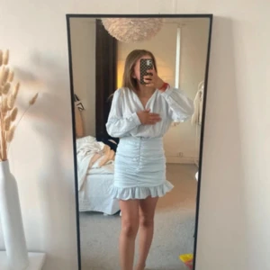 Ljusblå klänning från NLY Trend - Säljer en ljusblå klänning från NLY Trend med v-ringning och långa ärmar. Klänningen har en åtsittande passform med rynkdetaljer och volang vid fållen. Perfekt för en stilren look!