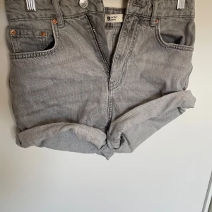 Grå jeansshorts från Gina - Säljer ett par grå jeansshorts från Gina Tricot. De har en klassisk design med fem fickor och uppvikta ben. Perfekta för en avslappnad stil. Den har en högre midja.