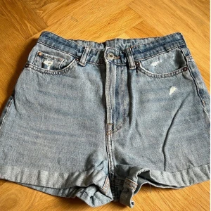 Blå jeansshorts - Säljer ett par blå jeansshorts med en loose fit och hög midja. Shortsen har slitna detaljer både fram och bak, vilket ger dem en cool och avslappnad look. Perfekta för sommardagar! 🩳Är avklippta och upplagda hemma 