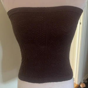 Brun tubtopp med  mönster  - Snygg brun tubtopp med vacker broderad design. Perfekt för en stilren look. Passar bra till både jeans och kjol. Aldrig använd, skicka EJ prisförslag