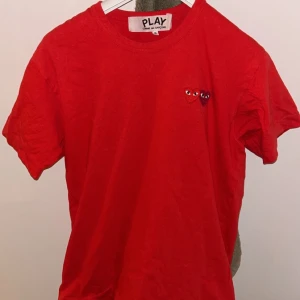 Röd t-shirt från Comme des Garçons Play - Säljer en snygg röd t-shirt från Comme des Garçons Play med det ikoniska hjärtmotivet på bröstet. T-shirten är kortärmad och gjord i mjuk bomull. Perfekt för en stilren och avslappnad look. Köpt på nordiska kompaniet för ca 1200