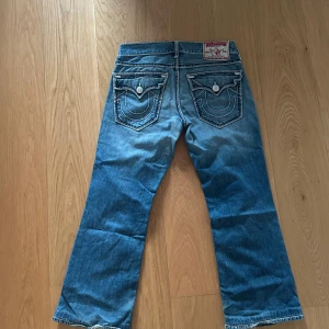 True Religion jeans - Säljer ett par blå jeans från True Religion med en cool slitning på. Dem är dekorerade med märkets ikoniska broderade fickor baktill. Perfekta för en avslappnad look. Fett snygga i helhet men mycket detalj - köpta från respektabel återförsäljare i irland (trueygarms) köpte de för 1300. Använts vardagligt finns syn på användning.