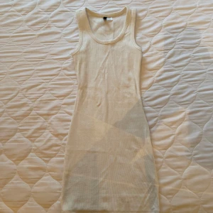 Vit  ribbad klänning - Säljer en vit ribbad klänning med ärmlös design. Perfekt för en minimalistisk look. Klänningen har en tight passform som framhäver figuren. Klänningen är stretchig. 