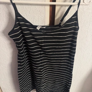 Svart- och vitrandig linne från H&M - Säljer ett svart linne med vita horisontella ränder från Hm. Linnet har smala axelband och är i en rak, enkel modell som passar perfekt till sommaren. Mjuk och lätt i materialet.